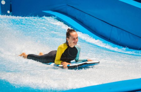 Foto de Hermosa joven surfeando en un simulador de olas en un parque de atracciones acuáticas. - Imagen libre de derechos