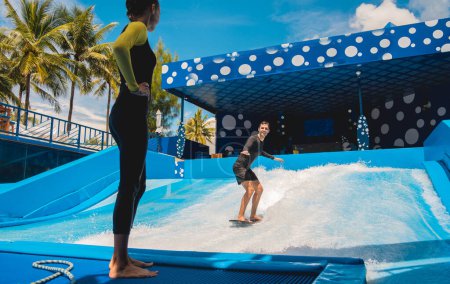 Foto de Joven surfeando con entrenador en un simulador de olas en un parque de atracciones acuático. - Imagen libre de derechos