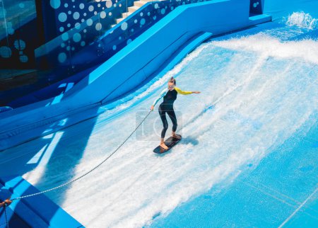 Foto de Hermosa joven surfeando en un simulador de olas en un parque de atracciones acuáticas. - Imagen libre de derechos