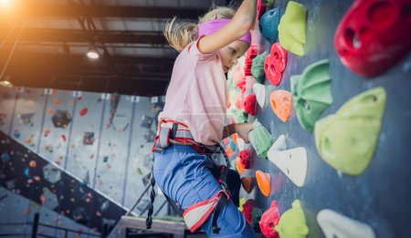 Téléchargez les photos : Un bébé grimpeur fort grimpe un mur artificiel avec des poignées et des cordes colorées - en image libre de droit