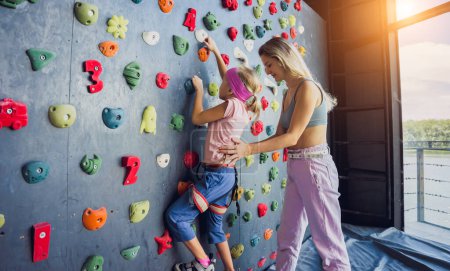 Téléchargez les photos : Un bébé grimpeur fort grimpe un mur artificiel avec des poignées et des cordes colorées - en image libre de droit