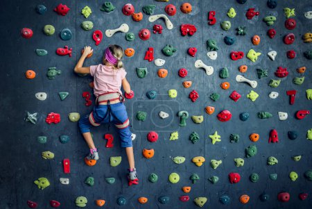 Photo for A strong baby climber climbs an artificial wall with colorful grips and ropes - Royalty Free Image