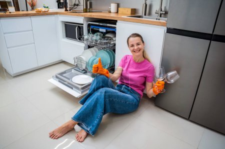Foto de Mujer joven sentada en el suelo cerca de la máquina lavavajillas. - Imagen libre de derechos