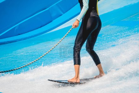Photo for Beautiful young woman surfing on a wave simulator at a water amusement park. - Royalty Free Image