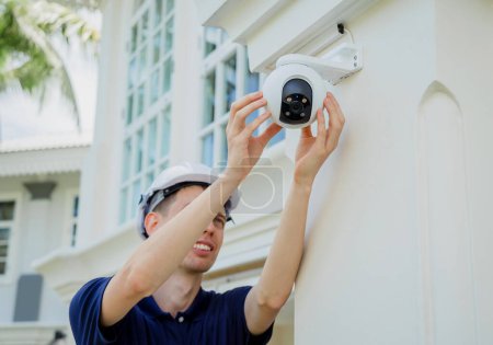 Téléchargez les photos : Un technicien installe une caméra de vidéosurveillance sur la façade d'un immeuble résidentiel - en image libre de droit