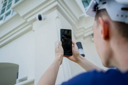 Téléchargez les photos : Un technicien installe une caméra de vidéosurveillance sur la façade d'un immeuble résidentiel - en image libre de droit