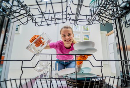 Téléchargez les photos : Jeune femme prend la vaisselle de la machine à laver le vaisselle. - en image libre de droit