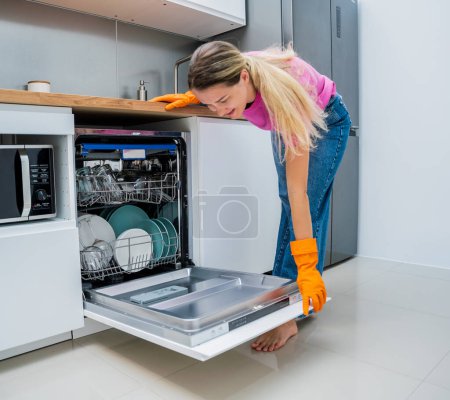 Photo for Young woman takes dishes out of the dishwasher machine. - Royalty Free Image