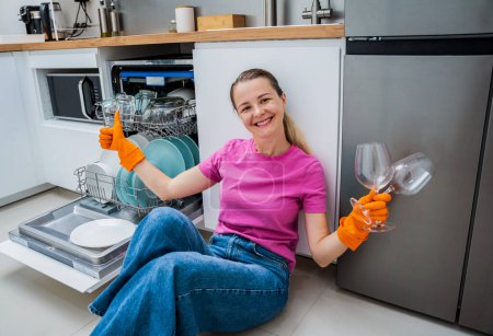 Photo for Young woman sitting on the floor near the dishwasher machine. - Royalty Free Image