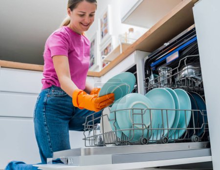 Photo for Young woman takes dishes out of the dishwasher machine. - Royalty Free Image