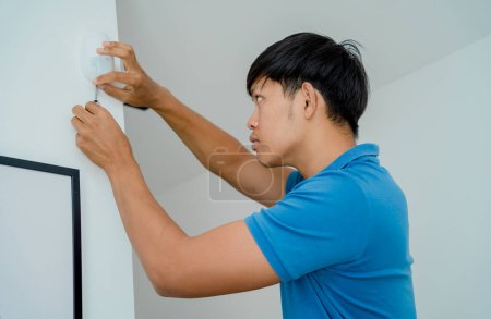 Téléchargez les photos : Un technicien installant un détecteur de mouvement dans un appartement moderne - en image libre de droit