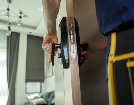 Foto de Un técnico instala una cerradura de puerta inteligente moderna en la puerta de madera. - Imagen libre de derechos