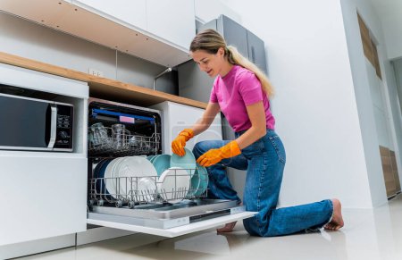 Foto de Mujer joven saca los platos de la máquina lavavajillas. - Imagen libre de derechos