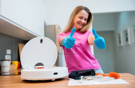 Photo for A young woman cleans a robot vacuum cleaner from dirt after cleaning - Royalty Free Image