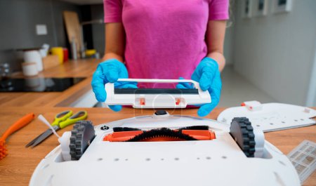 Foto de Una joven limpia una aspiradora robot de la suciedad después de la limpieza - Imagen libre de derechos