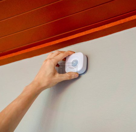 Foto de Un técnico instala un detector de movimiento moderno en un acogedor apartamento. - Imagen libre de derechos