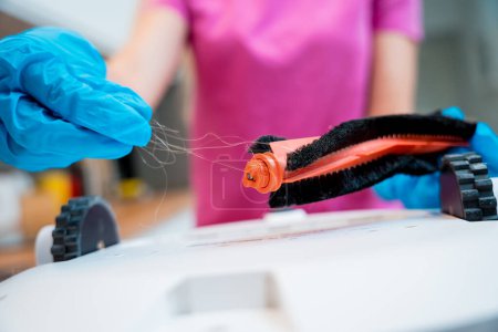 Téléchargez les photos : Une jeune femme nettoie un robot aspirateur de la saleté après le nettoyage - en image libre de droit