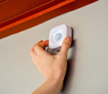 Téléchargez les photos : Un technicien installe un détecteur de mouvement moderne dans un appartement confortable. - en image libre de droit