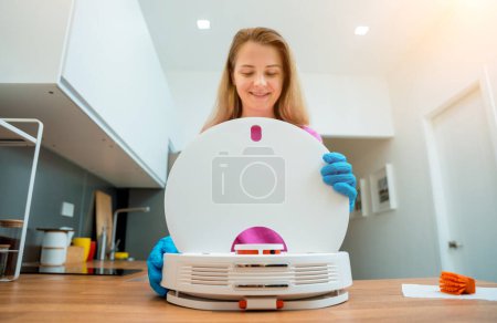 Foto de Una joven limpia una aspiradora robot de la suciedad después de la limpieza - Imagen libre de derechos
