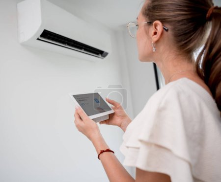Téléchargez les photos : Jeune femme exploite un système de climatisation sans fil dans un appartement moderne - en image libre de droit