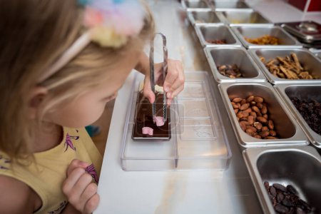 Téléchargez les photos : Bébé fille dans l'atelier lors d'une leçon sur la fabrication de chocolats et de bonbons faits à la main. - en image libre de droit