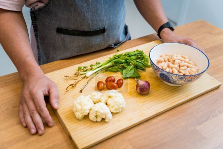 Cutting board with ingredients for preparing bean porridge with cauliflower and vegetables.