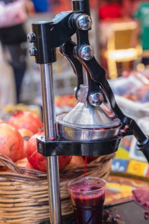 Squeeze juice from fresh pomegranates using a manual press at a street food market