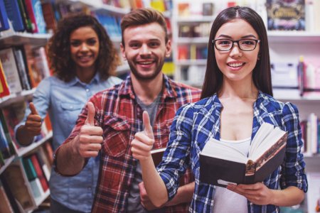 Photo for Young people are holding books, showing Ok sign and smiling while standing at the bookshop one by one, attractive girl in the foreground - Royalty Free Image
