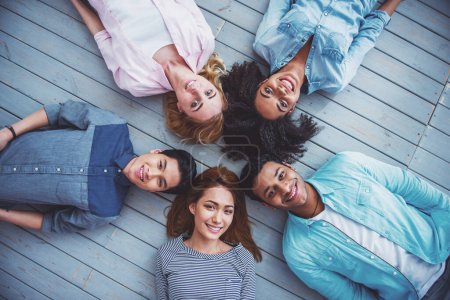 Foto de Vista superior de jóvenes de diferentes nacionalidades mirando a la cámara y sonriendo tumbados en el suelo - Imagen libre de derechos