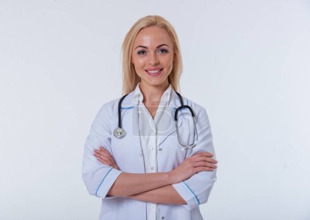 Foto de Retrato de una hermosa doctora de bata blanca mirando a la cámara y sonriendo de pie con los brazos cruzados, aislada sobre fondo blanco - Imagen libre de derechos