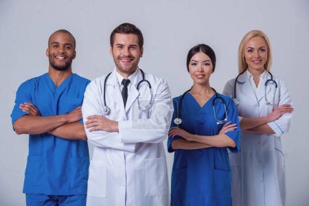 Photo for Group of medical doctors of different nationalities and genders is looking at camera and smiling, standing with crossed arms on gray background - Royalty Free Image