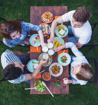 Foto de Vista superior de la gente joven hermosa tintineo vasos mientras se sienta a la mesa y tener picnic al aire libre - Imagen libre de derechos