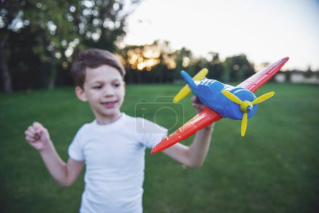 Téléchargez les photos : Beau petit garçon tient un avion jouet et sourit tout en jouant à l'extérieur. Jouet en bref - en image libre de droit