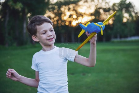 Téléchargez les photos : Beau petit garçon tient un avion jouet et sourit tout en jouant à l'extérieur - en image libre de droit