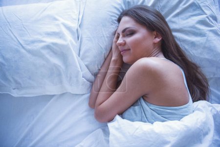 Téléchargez les photos : Vue du dessus de la belle jeune femme souriante tout en dormant dans le lit - en image libre de droit