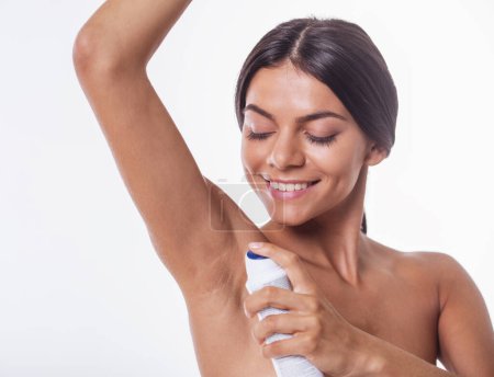 Téléchargez les photos : Portrait de belle fille nue utilisant un déodorant spray et souriant, isolé sur blanc - en image libre de droit