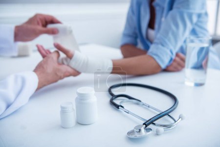 geschnittenes Bild eines Arztes, der der Frau bei der Arbeit in seinem Büro die lädierte Hand bandagiert