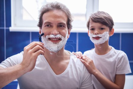 Téléchargez les photos : Père et fils sourient tout en se rasant dans la salle de bain - en image libre de droit