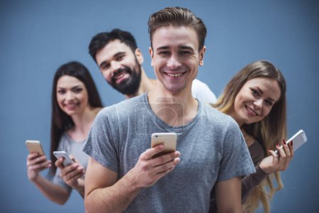 Beaux jeunes gens utilisent des smartphones et souriant, sur fond gris
