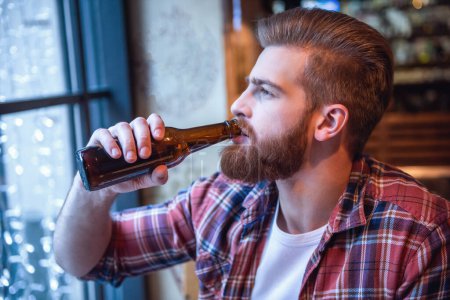Téléchargez les photos : Beau barbu homme boit de la bière tout en se reposant dans un pub - en image libre de droit