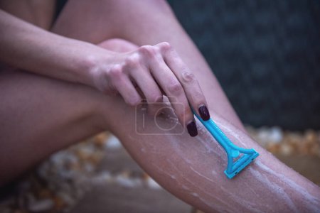 Foto de Imagen recortada de la hermosa chica afeitándose las piernas con una navaja de afeitar mientras toma la ducha en el baño - Imagen libre de derechos