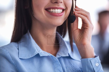 Téléchargez les photos : Image recadrée d'une femme d'affaires attrayante dans un casque parlant et souriant tout en travaillant au bureau - en image libre de droit