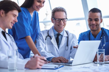 Téléchargez les photos : Les médecins qui réussissent utilisent un ordinateur portable et sourient tout en discutant - en image libre de droit