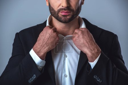 Téléchargez les photos : Image recadrée d'un bel homme d'affaires en costume ajustant son col, sur fond gris - en image libre de droit