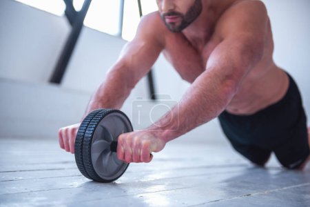 Foto de Imagen recortada de un hombre musculoso guapo con torso desnudo haciendo ejercicio con rueda de ejercicio - Imagen libre de derechos