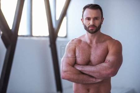 Foto de Hombre musculoso guapo con torso desnudo está mirando a la cámara mientras está de pie con los brazos cruzados en el gimnasio - Imagen libre de derechos