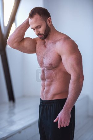 Foto de Retrato de un hombre musculoso guapo con torso desnudo de pie con los brazos cruzados en el gimnasio - Imagen libre de derechos