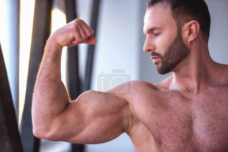 Foto de Hombre musculoso guapo con torso desnudo está mostrando sus músculos mientras está de pie en el gimnasio - Imagen libre de derechos