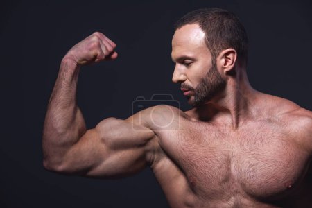 Foto de Hombre musculoso guapo con torso desnudo mostrando músculos mientras posa en la cámara, sobre fondo oscuro - Imagen libre de derechos