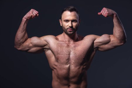 Photo for Handsome muscular man with bare torso showing muscles while posing at camera, on dark background - Royalty Free Image